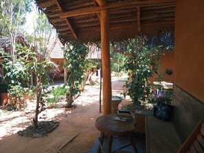 Un espacio exterior cubierto con una mesa y sillas, rodeado de plantas en macetas y un edificio rústico.