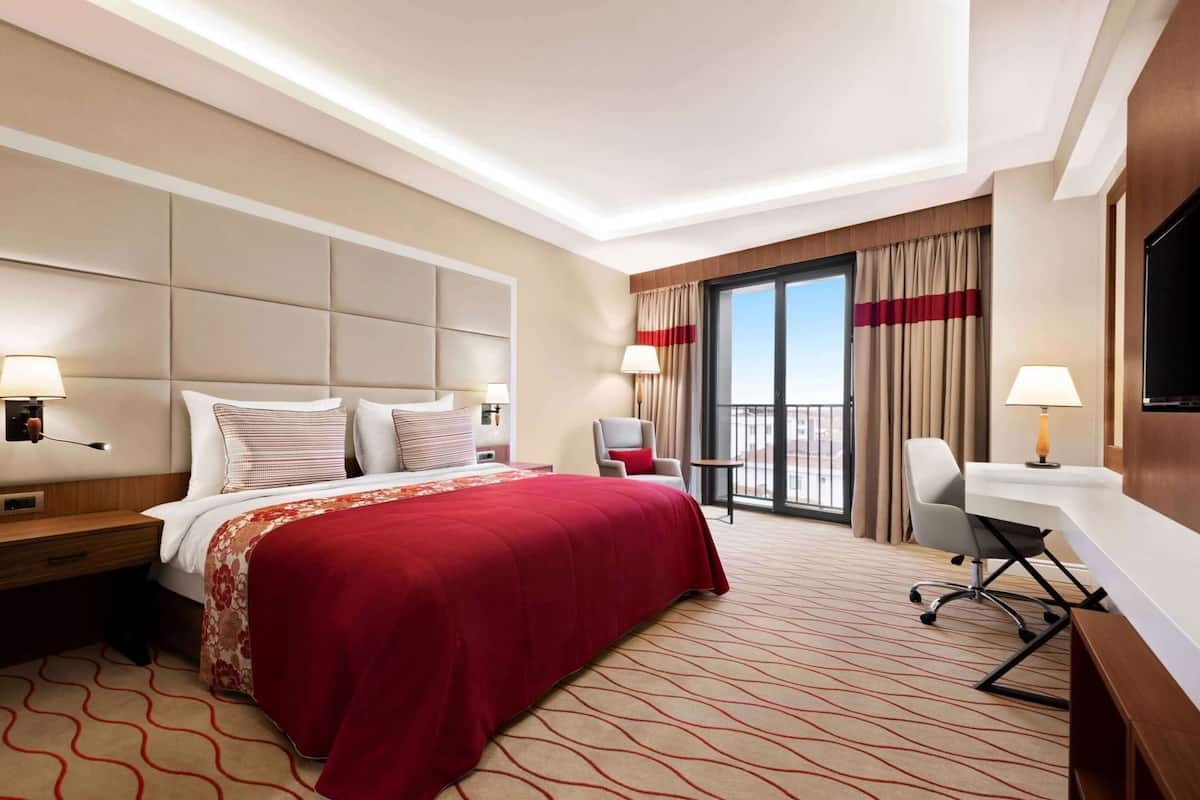 Een hotelkamer met een bed, een bureau, een stoel, een televisie en een balkon met gordijnen.