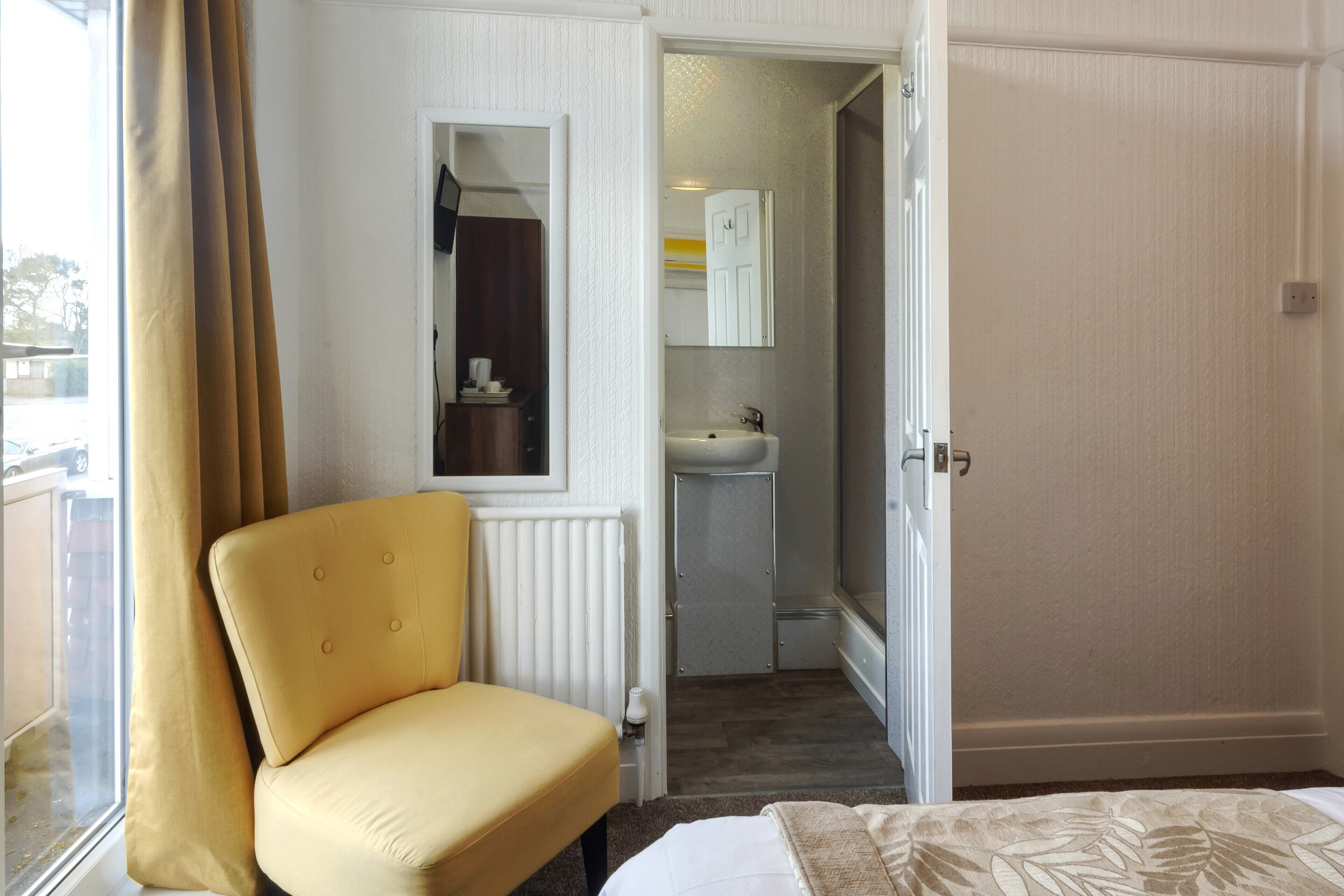 A room with a yellow chair, a bed, a bathroom with a sink, and a door leading to another room.