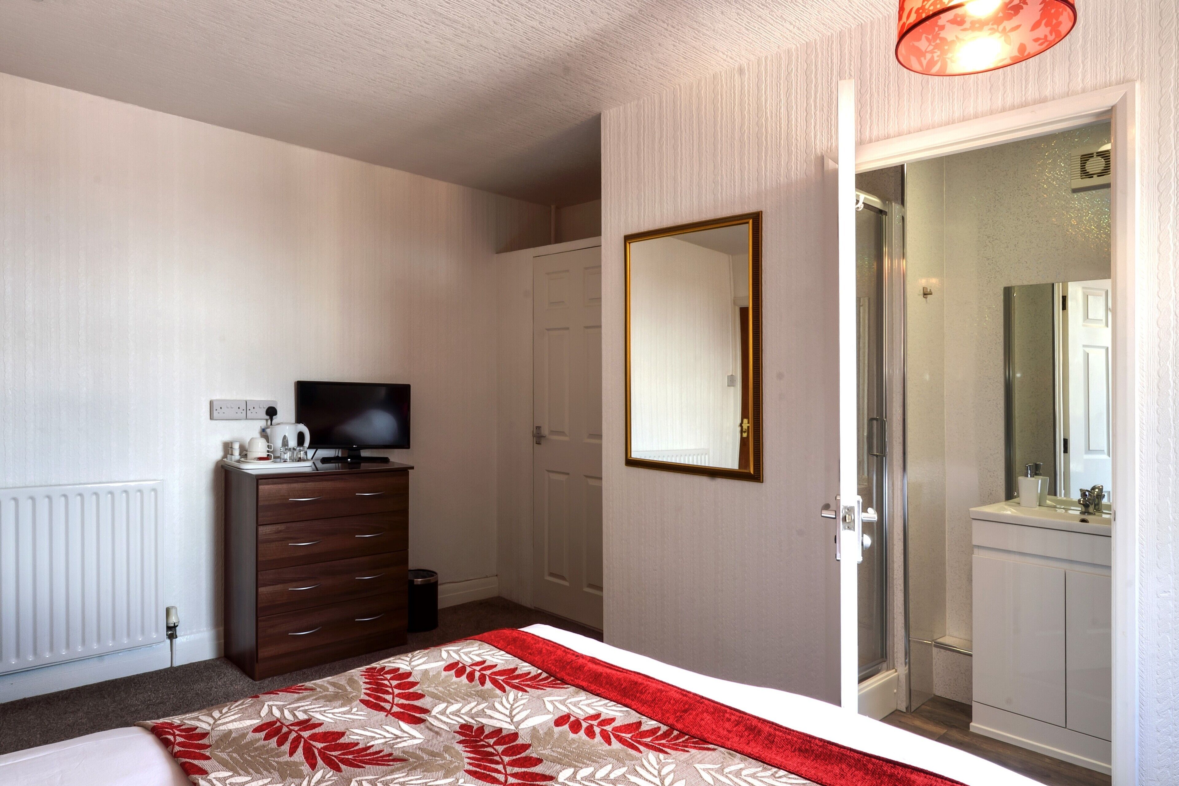 A bedroom with a bed, dresser, television, and a bathroom visible through an open door.