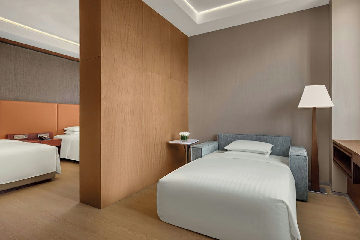 A modern hotel room with a large bed, a smaller bed, a desk, and a nightstand.