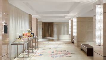 Un couloir orné d’un tapis à motifs floraux, une table de buffet garnie de plats et un banc.