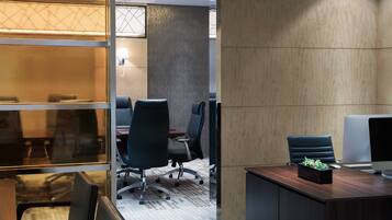 A conference room with a glass partition, a wooden desk with a computer, and office chairs.