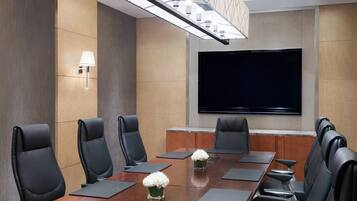 Una sala de conferencias con una gran mesa, sillas de cuero negro, un televisor de pantalla plana y una lámpara moderna.