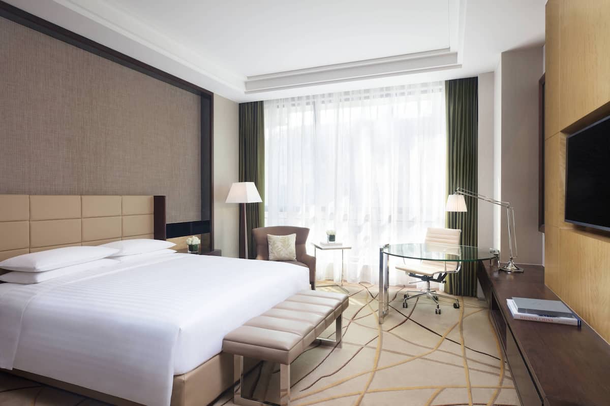A hotel room with a large bed, a desk, a chair, a lamp, and a TV.
