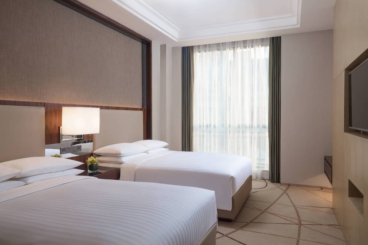 A hotel room with two beds, a TV, a nightstand, and a window with curtains.