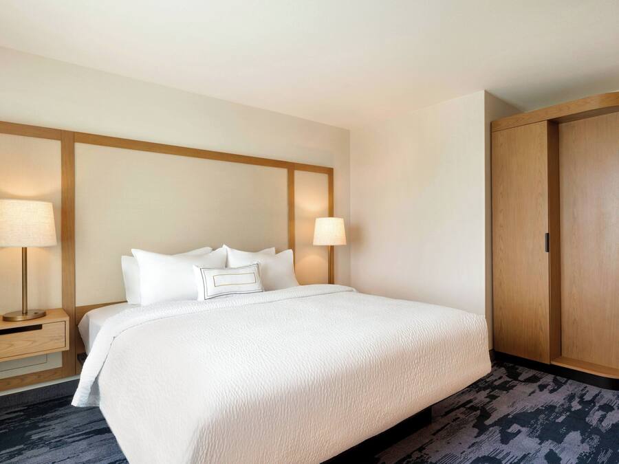 A hotel room with a large bed, two bedside lamps, a wooden wardrobe, and a nightstand with a lamp.