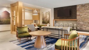 A modern living room with a round wooden coffee table, two green upholstered chairs, a white sofa, and a stone accent wall. - Fairfield Inn & Suites by Marriott Boulder Longmont (Longmont)
