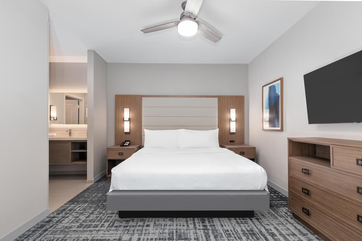Una camera d'albergo moderna con un ampio letto, una testiera in legno, lampade sui comodini, una TV a schermo piatto e una ventola a soffitto.