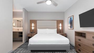 Moderni hotellihuone, jossa on suuri sänky, puinen pääty, yöpöytävalaisimet, taulutelevisio ja kattotuuletin.
