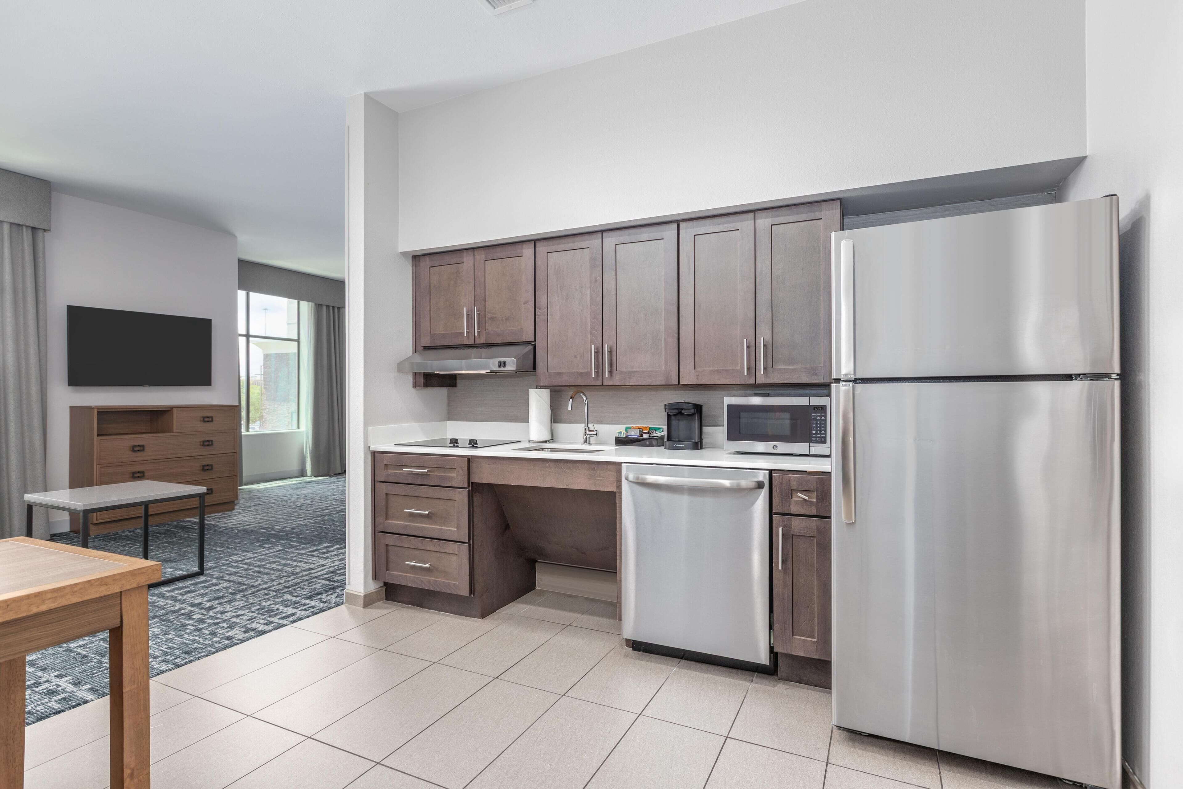 A modern kitchen with stainless steel appliances, wooden cabinets, and a flat-screen TV.