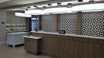 A modern hotel reception area with a wooden reception desk, a minibar, and a patterned wall.