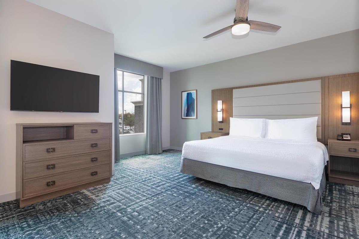 Camera d'albergo con un letto grande, una TV a schermo piatto fissata al muro, una ventola a soffitto e vista all'esterno attraverso una grande finestra.
