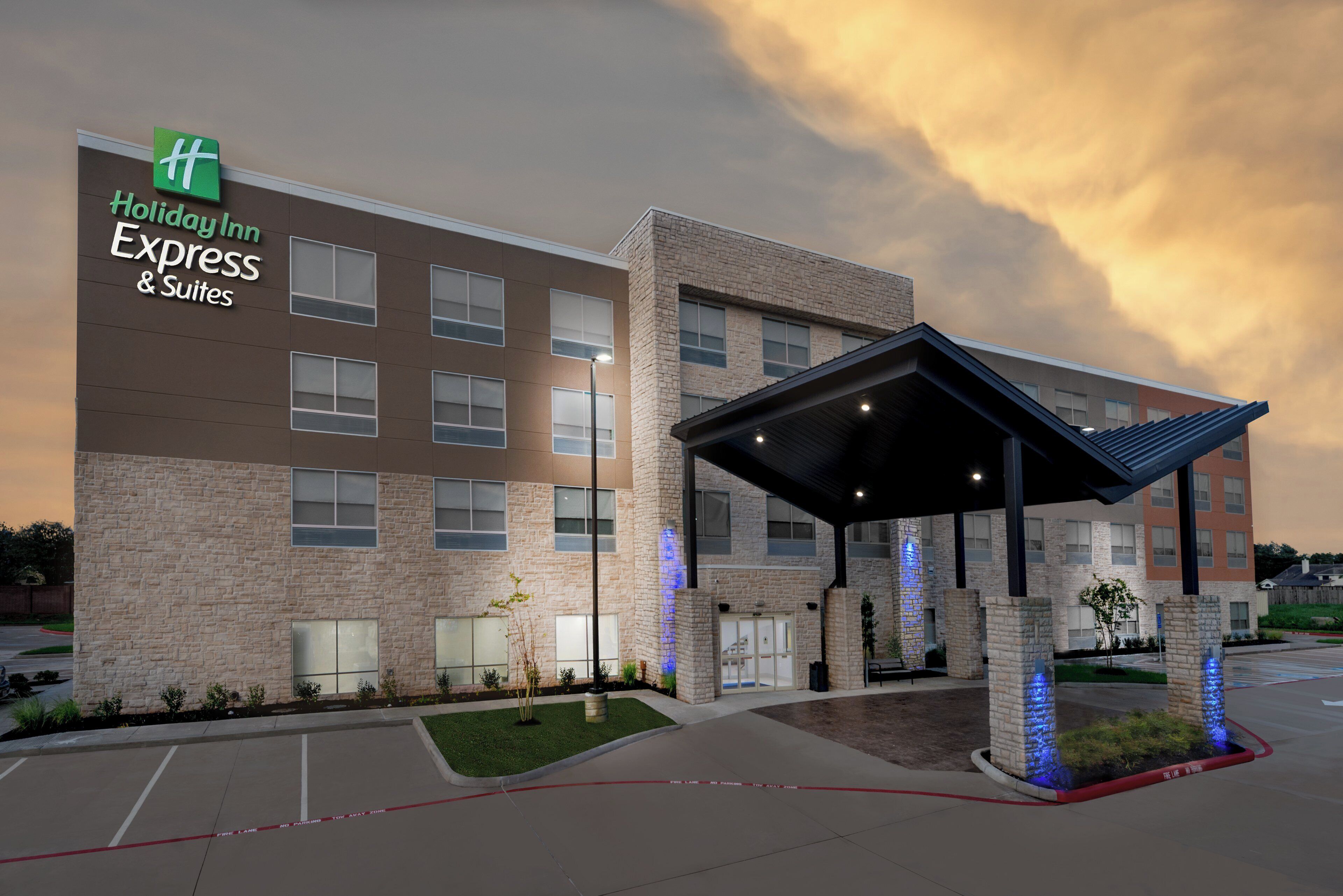 Ein Holiday Inn Express & Suites Gebäude mit Ziegelverkleidung, einem überdachten Eingang und einem Parkplatz.