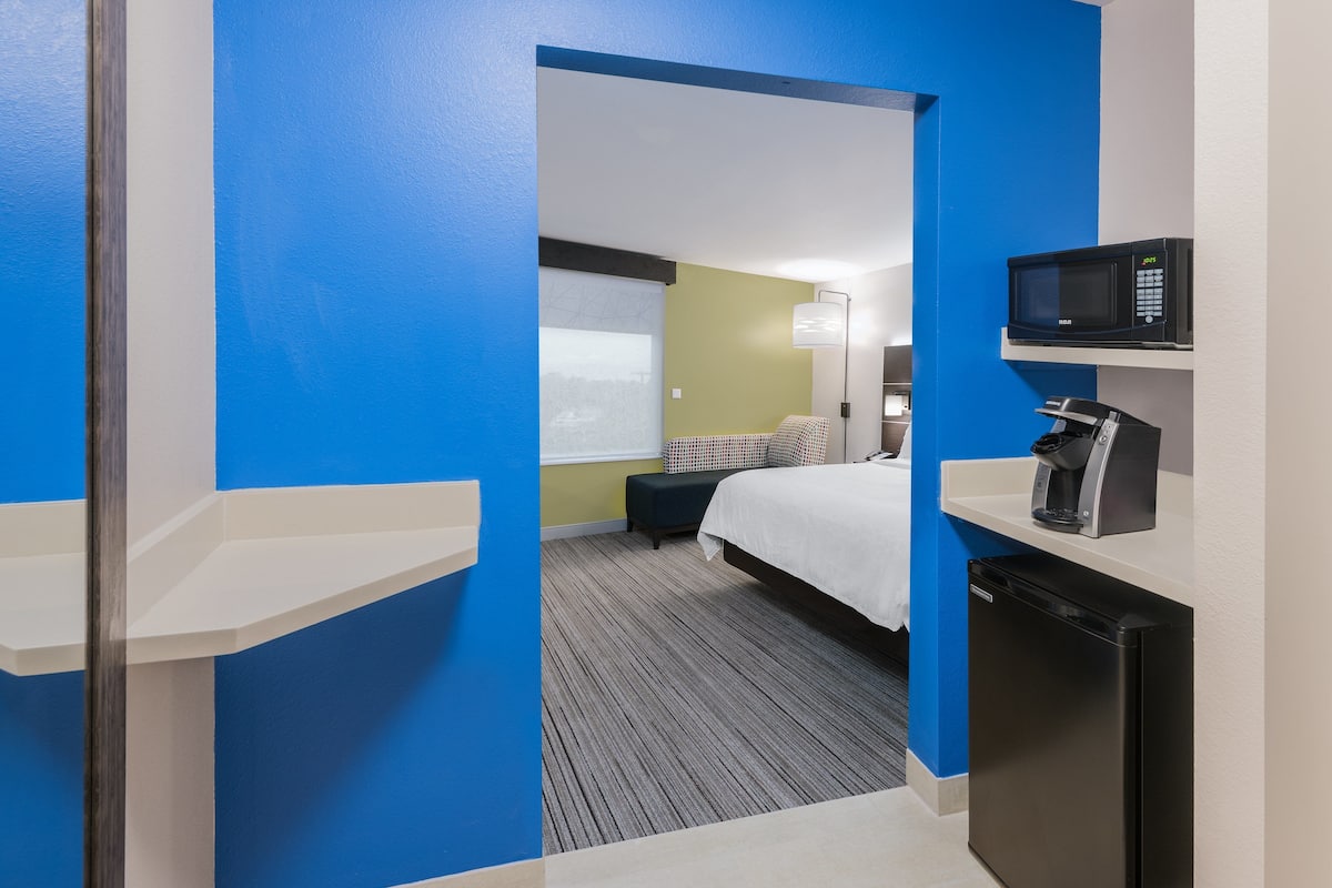 A hotel room with a bed, a desk with a microwave, a coffee maker, and a small refrigerator.