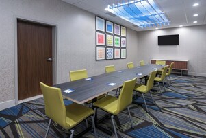Un salón de conferencias con una mesa larga, sillas amarillas, obras de arte enmarcadas en la pared y un televisor de pantalla plana.