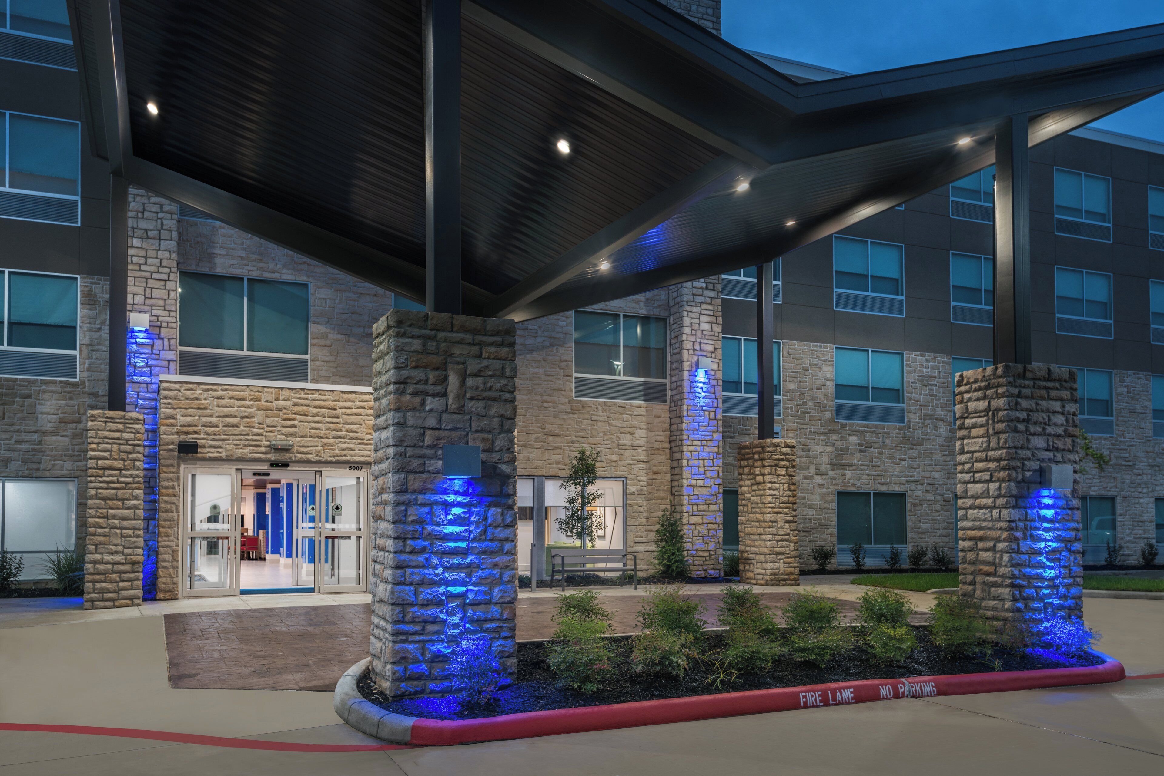 A building with a stone facade, a covered entrance, and blue lighting accents.