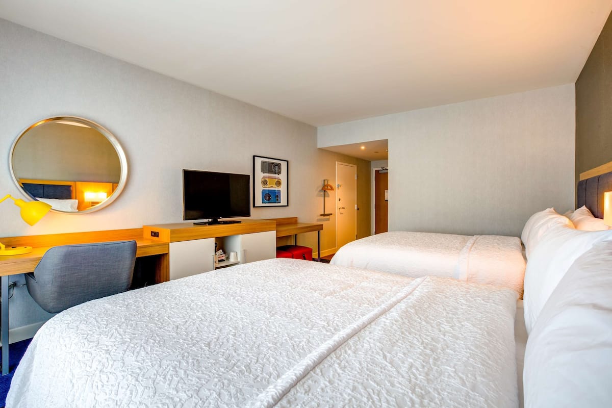 A hotel room with two beds, a desk with a computer, a TV, and a mirror.