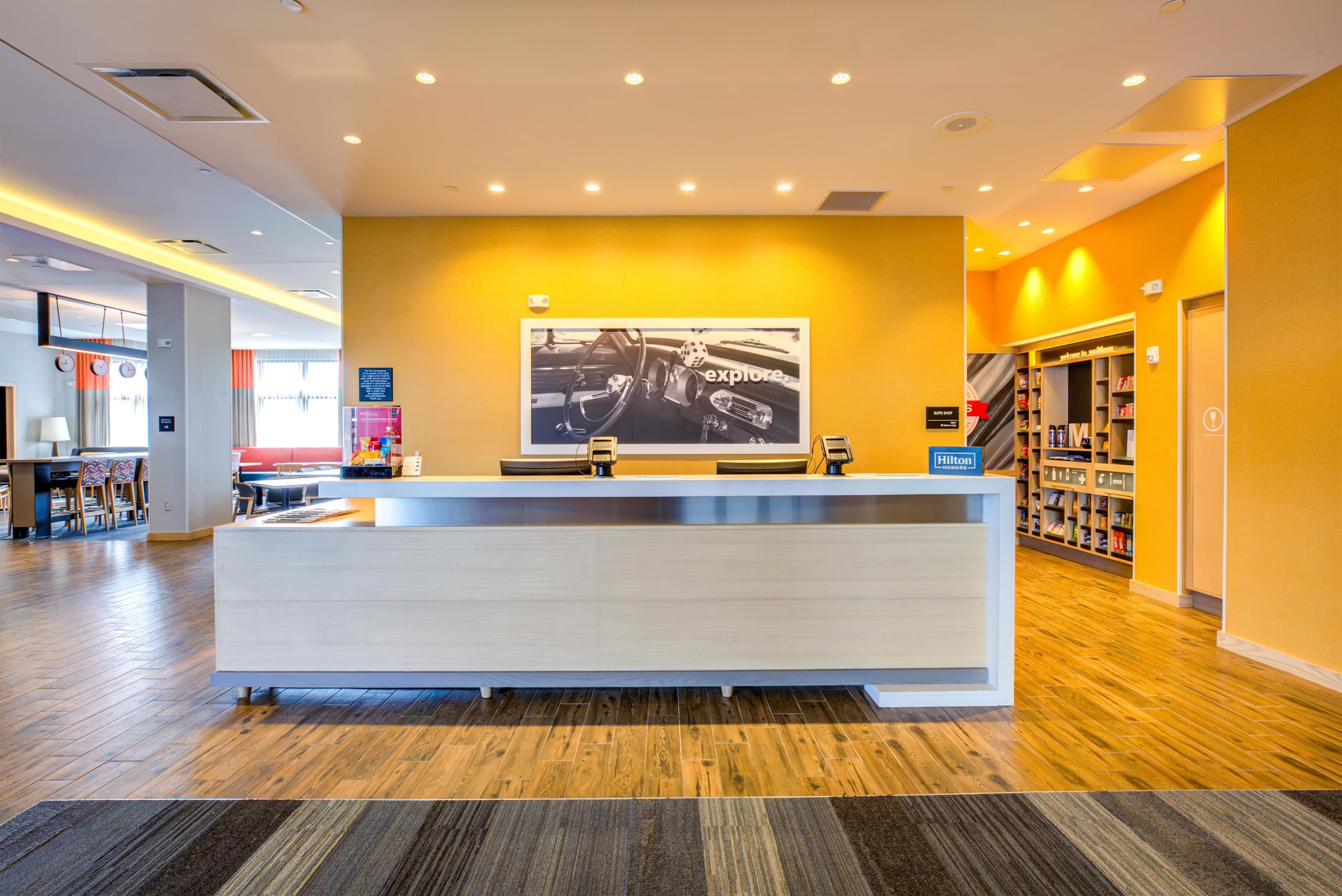 A hotel reception area with a modern design, featuring a reception desk, a large framed photograph on the wall, and a visible suite shop sign.