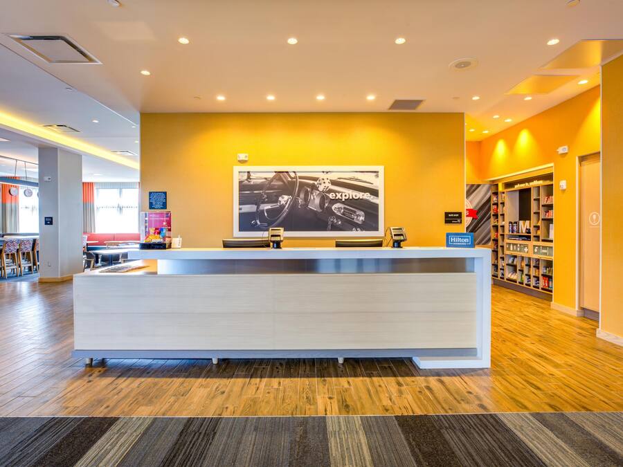 A hotel reception area with a modern design, featuring a reception desk, a large framed photograph on the wall, and a visible suite shop sign.