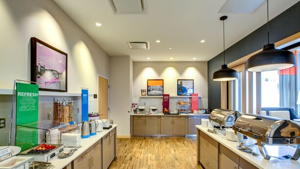 A modern kitchen with a wooden floor, equipped with coffee makers, a kettle, and a fruit bowl.
