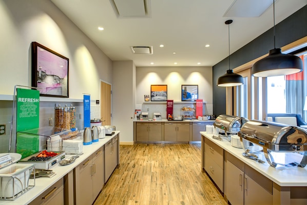 A modern kitchen with a wooden floor, equipped with coffee makers, a kettle, and a fruit bowl.