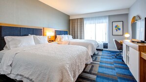 Une chambre d’hôtel avec deux lits, un bureau, une chaise, une télévision et une fenêtre avec des rideaux.