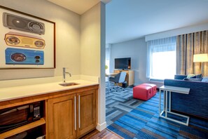 Ein Hotelzimmer mit Küchenzeile, einem Flachbildfernseher, einem Sofa, einem roten Hocker und einem gemusterten Teppich.