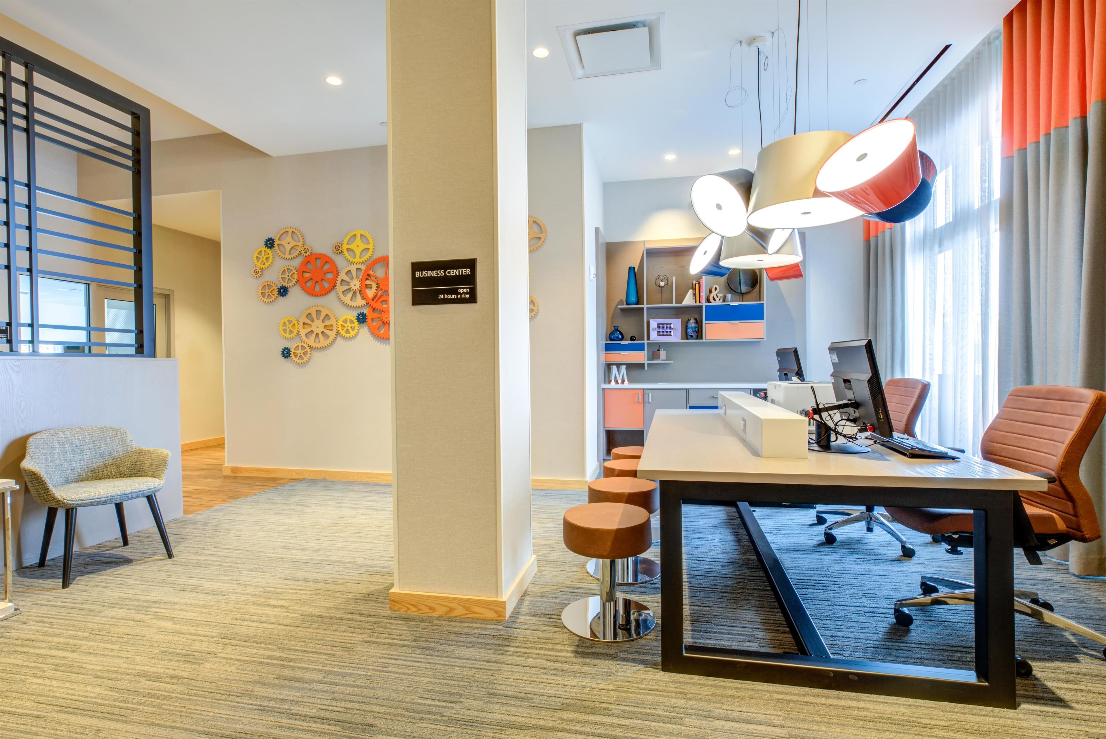 A modern office space with a desk, chairs, a bulletin board, and a sign indicating a business center.