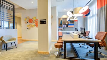 A modern office space with a desk, chairs, a bulletin board, and a sign indicating a business center.