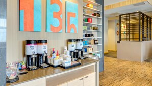 A modern hotel lobby with a coffee station, a reception desk, and a wall with large numbers.