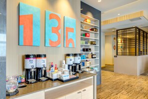 A modern hotel lobby with a coffee station, a reception desk, and a wall with large numbers. - Hampton Inn & Suites Boston/Waltham (Waltham)
