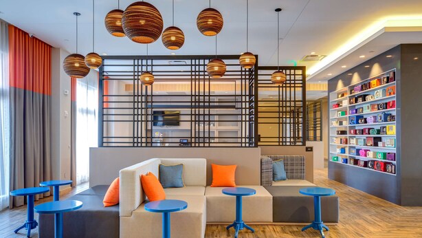 Un hall d’entrée moderne avec un canapé d’angle, des tables rondes bleues et une étagère où sont exposés des objets colorés.