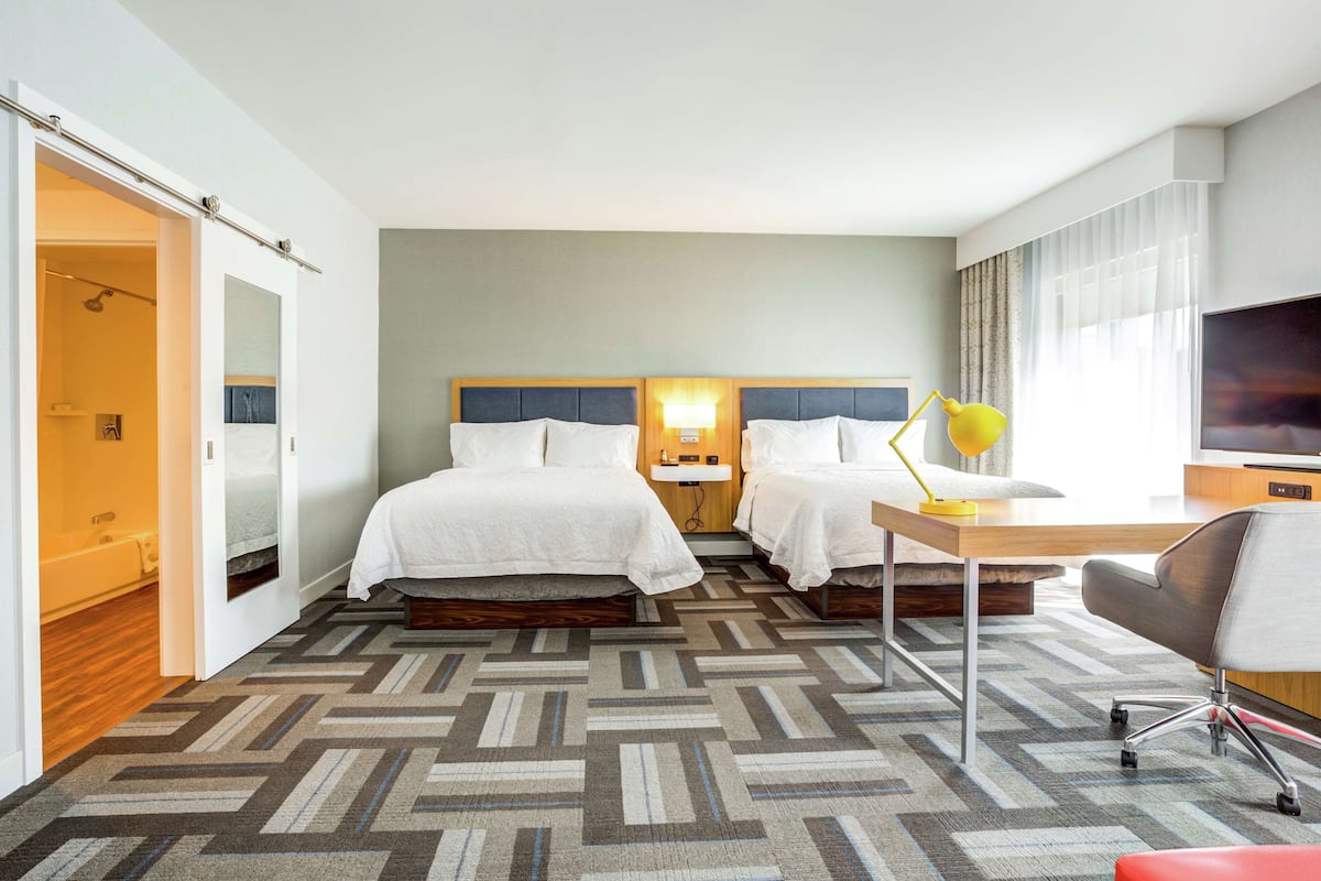 A hotel room with two beds, a desk with a lamp, a chair, and a TV.