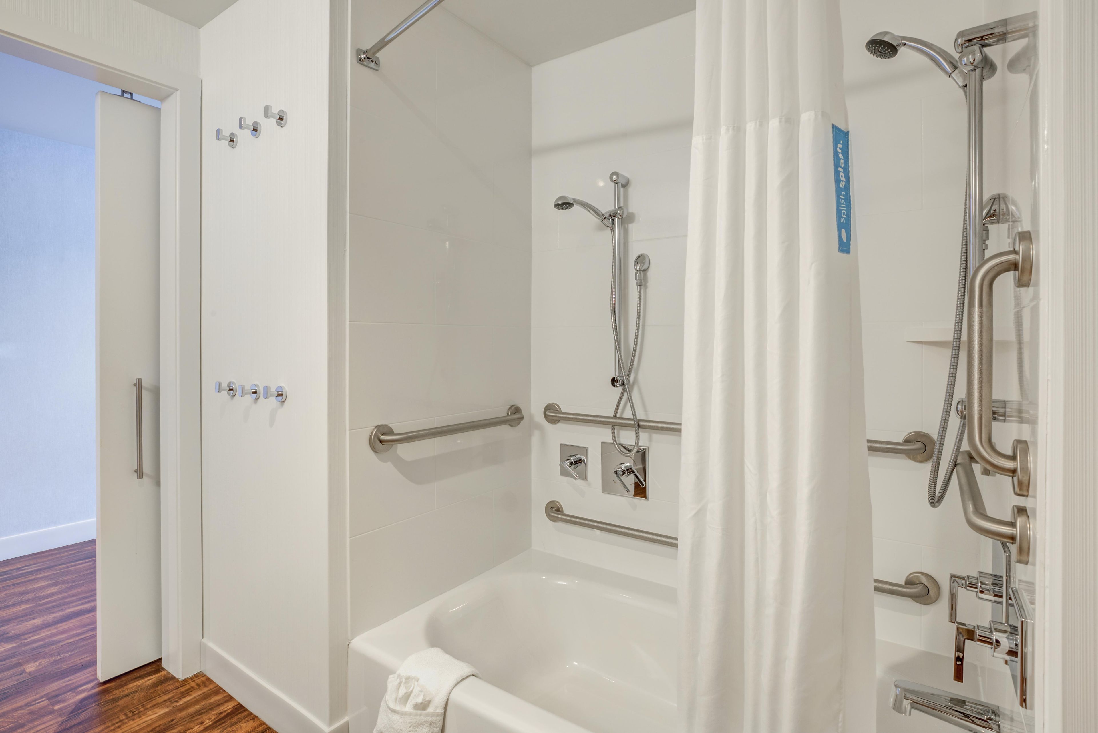 A bathroom with a bathtub, a shower, and a toilet. There are grab bars installed for safety.