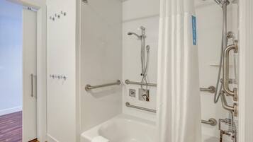 A bathroom with a bathtub, a shower, and a toilet. There are grab bars installed for safety.