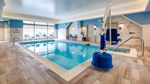 Une piscine intérieure avec un panneau indiquant qu’il est interdit de plonger, un poste de surveillance pour le sauveteur et un ascenseur accessible aux personnes en fauteuil roulant.