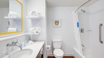 Een moderne badkamer met een wit wastafelmeubel, toilet en bad. Handdoeken liggen op een plank en er hangt een ingelijste foto aan de muur.