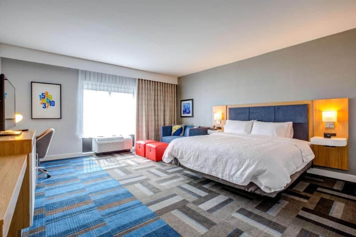 A hotel room with a large bed, a desk, a chair, a sofa, and a window with curtains.