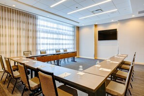 A conference room with a long table, chairs, a flat-screen TV, and a large window with blinds. - Hampton Inn & Suites Boston/Waltham (Waltham)