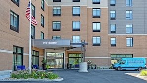 A modern building with a 'Welcome' sign, a flag, and a blue van parked in front.
