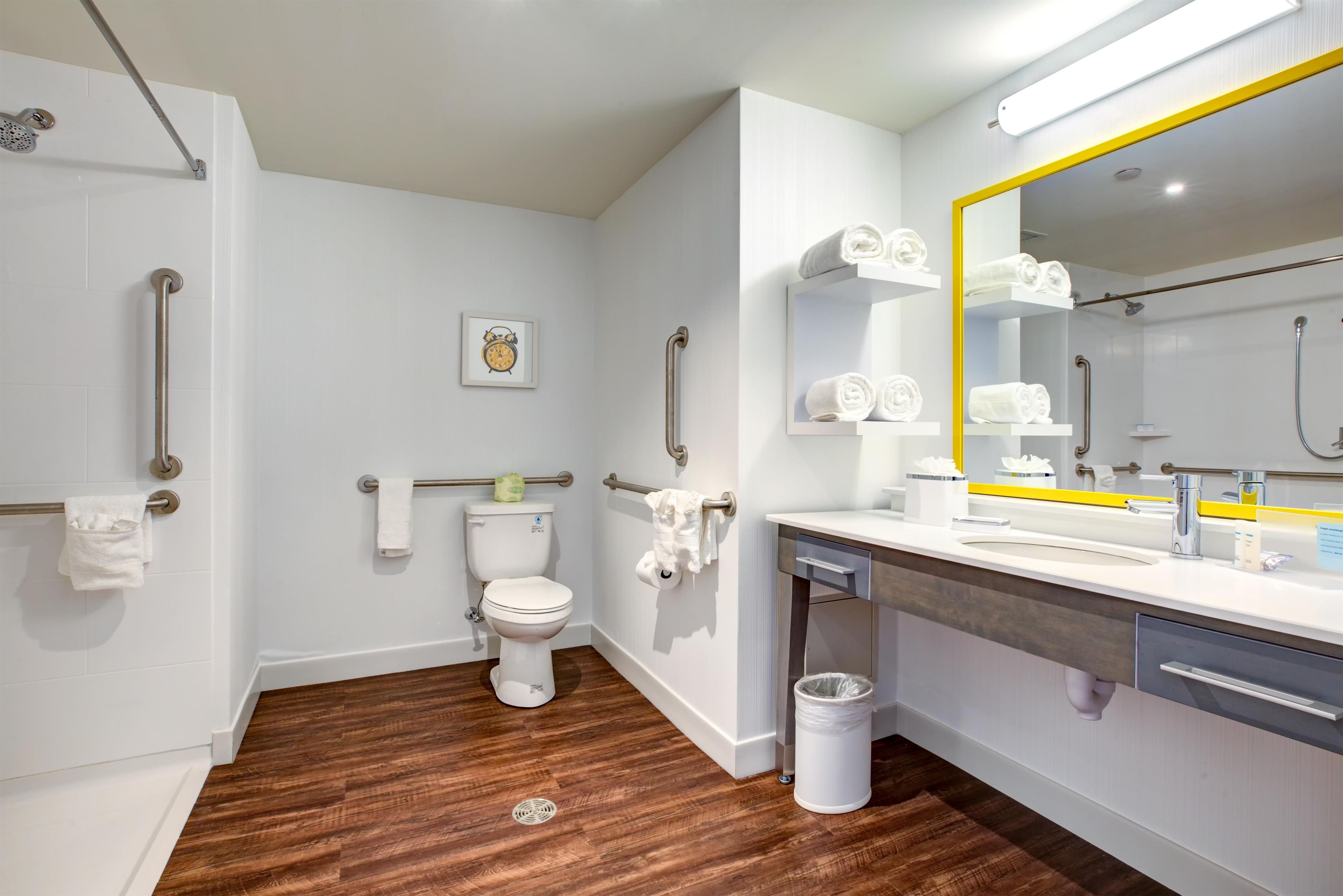 Une salle de bain moderne équipée de toilettes, d’un bidet, de barres d’appui, d’un lavabo avec un miroir et d’une poubelle.
