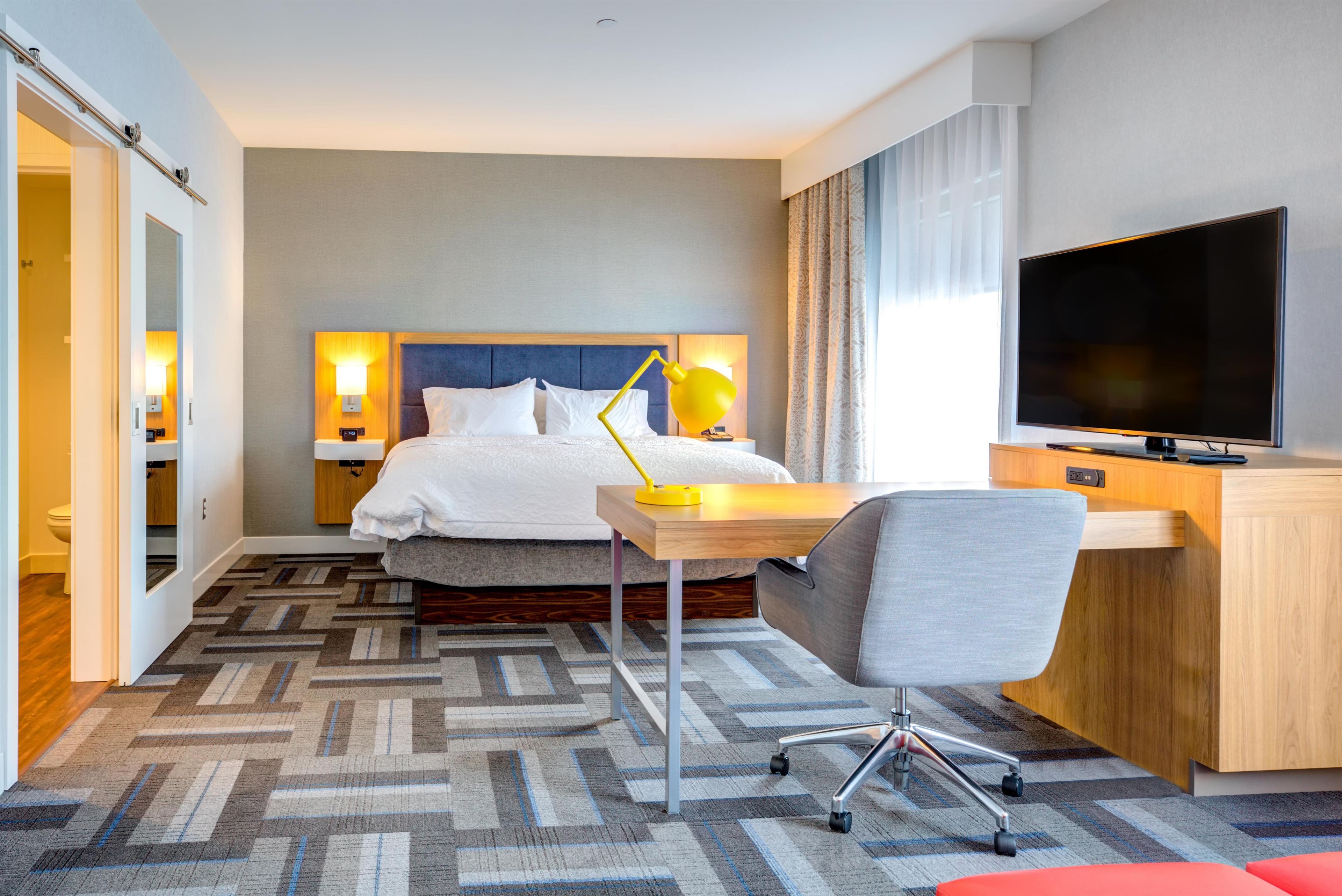 Ein Hotelzimmer mit Bett, Nachttischen, Schreibtisch, Stuhl, Fernseher und einem gemusterten Teppich.