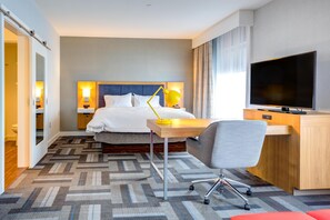 Ein Hotelzimmer mit Bett, Nachttischen, Schreibtisch, Stuhl, Fernseher und einem gemusterten Teppich.