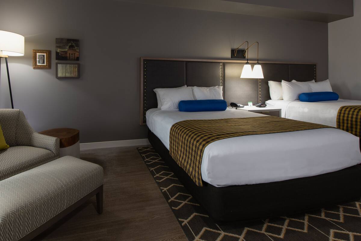 Une chambre d’hôtel avec deux lits, un canapé, une table d’appoint et une lampe.