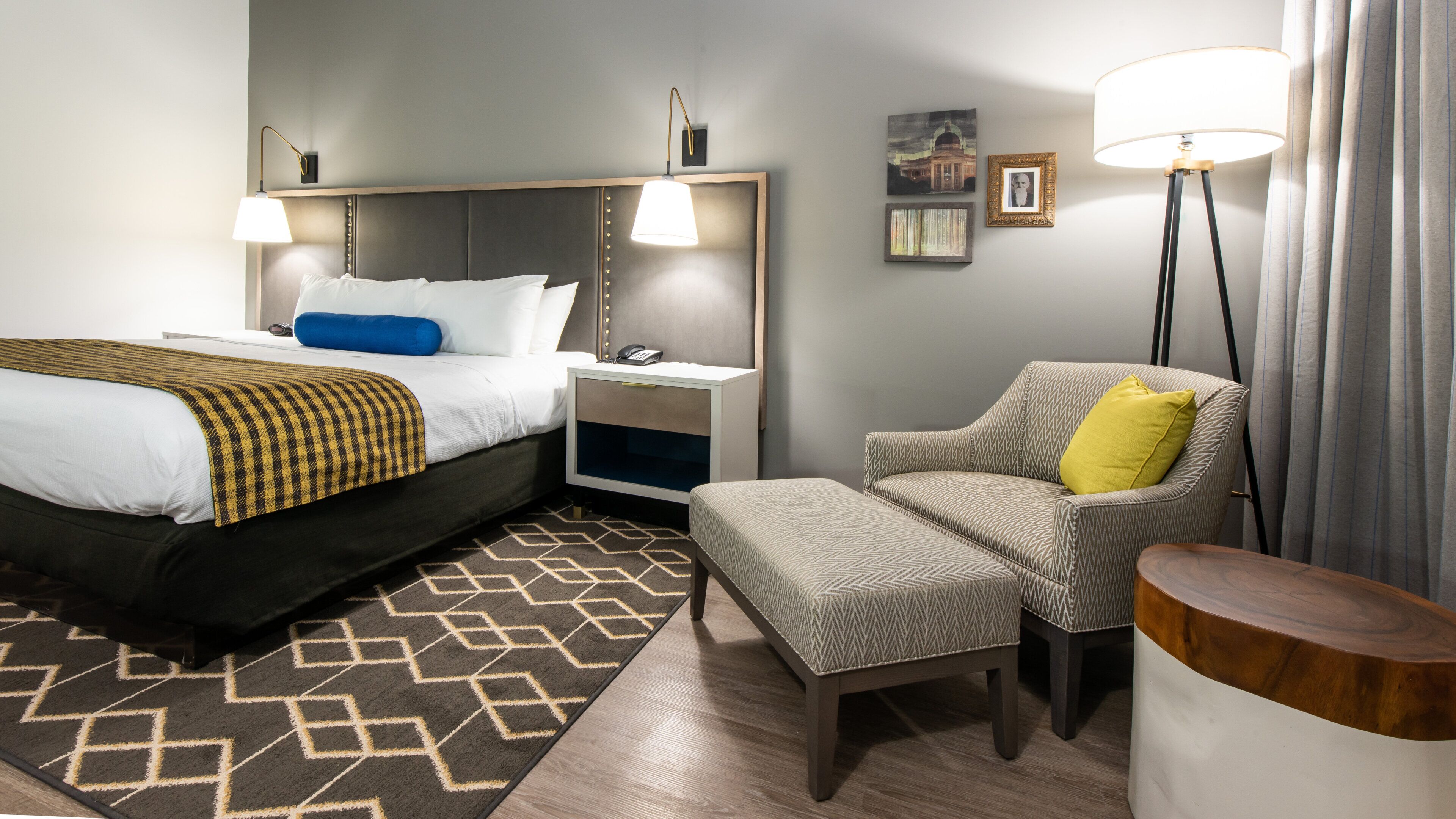 Una camera d'albergo con un letto, comodini, una sedia, una lampada e un tappeto.