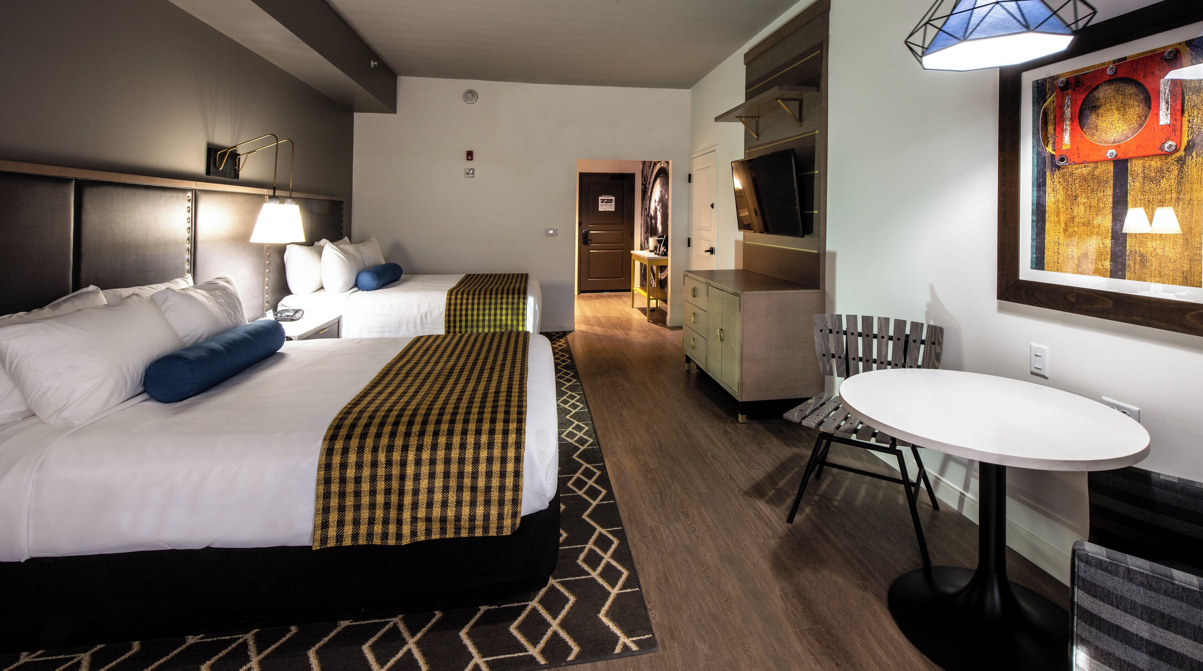 Habitación de hotel con dos camas, un escritorio, una silla, un televisor y una mesa de comedor.