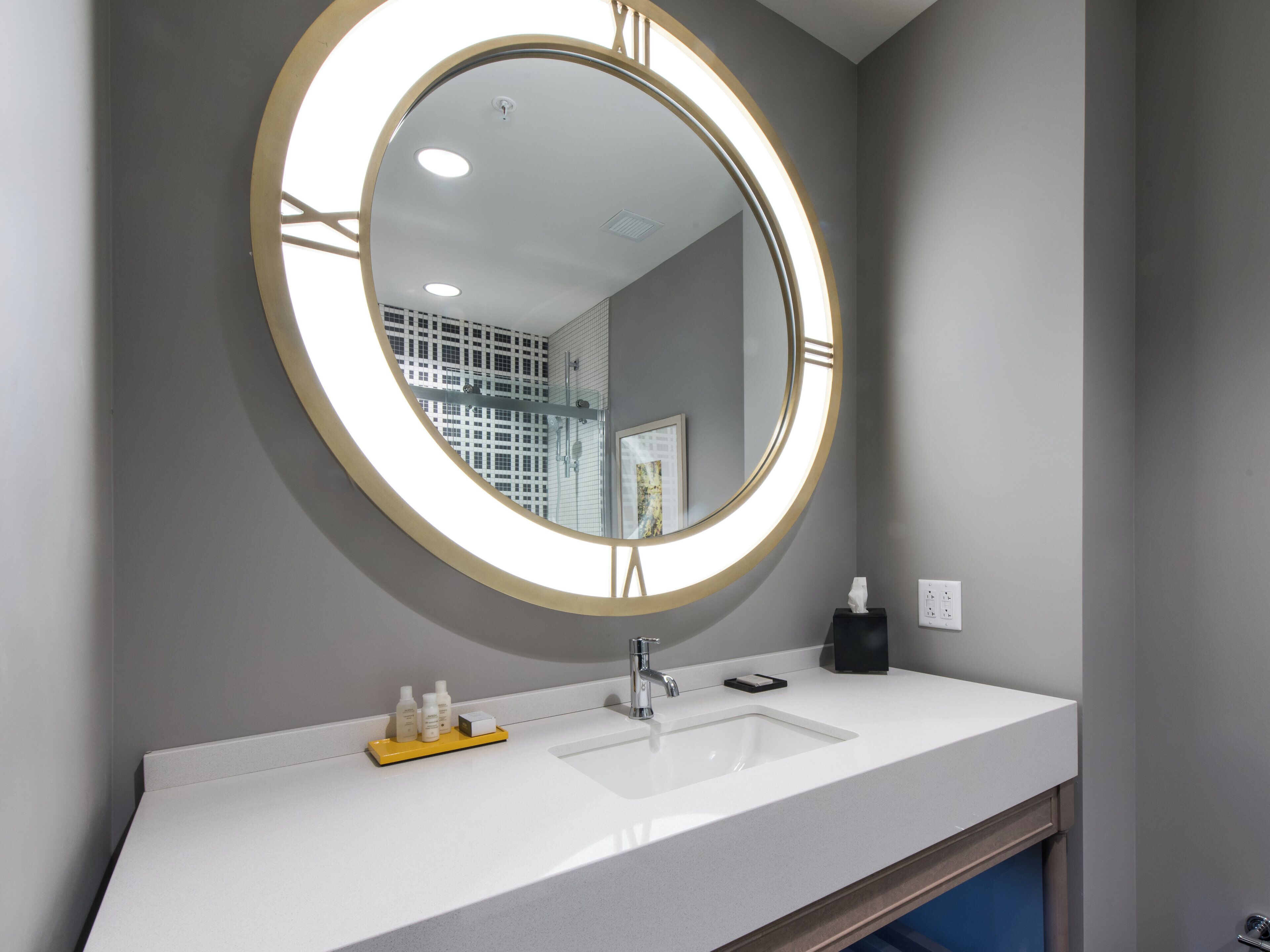 Une salle de bain avec un miroir rond, un lavabo et des articles de toilette.
