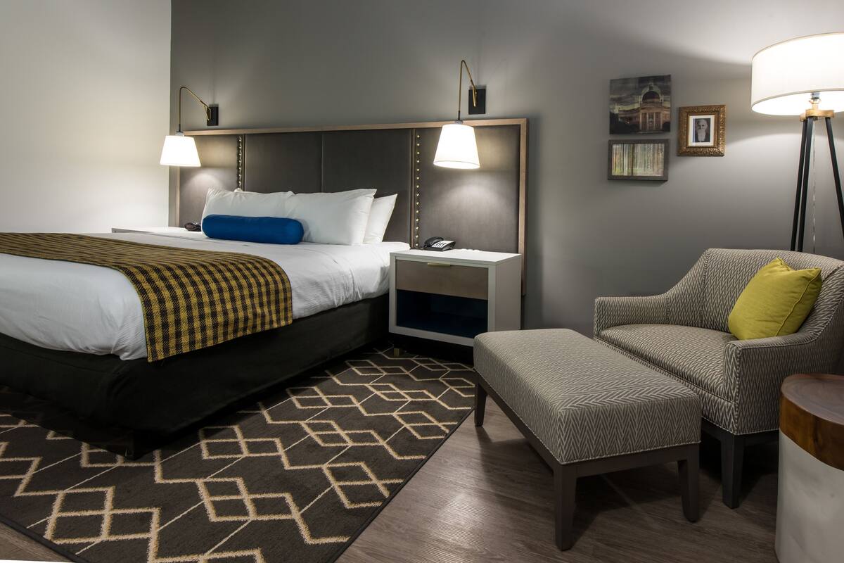 Une chambre d’hôtel avec un lit, des tables de chevet, une chaise, une lampe et un tapis.
