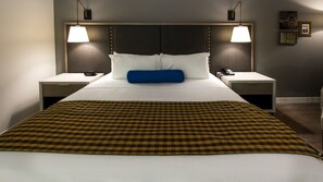 A hotel room with a large bed, two bedside tables, two lamps, a blue pillow, and a patterned throw blanket. - Hotel Indigo Hattiesburg by IHG (Hattiesburg)
